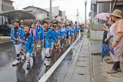 住民に見守られ、雨の中を進む子ど...